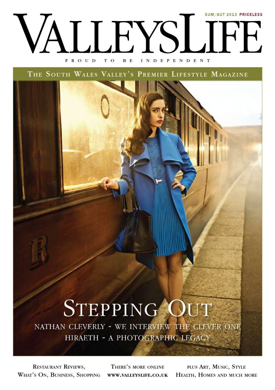 Valleys Life Summer/Autumn 2013 cover. A model with long wavy auburn hair wears a bright blue coat over a pleated blue dress and carries a black leather bag, leaning against a vintage wooden railway carriage on a platform in low golden light. Headline: Stepping Out.